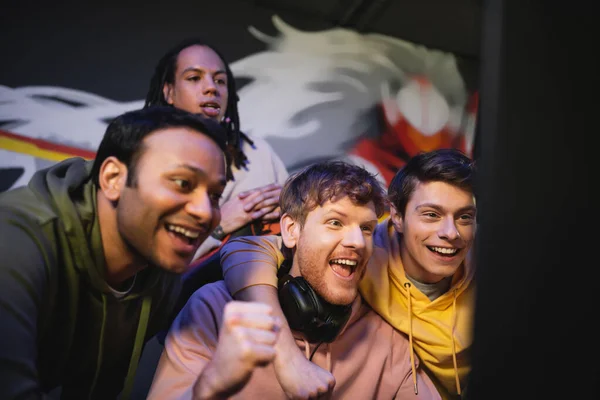 Jogadores multiétnicos excitados olhando para monitor de computador no clube de jogos — Fotografia de Stock