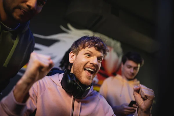 Homem excitado com fones de ouvido perto de amigos inter-raciais no clube de jogos — Fotografia de Stock
