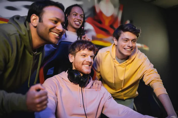 Carefree interracial team looking away near friend with headphones in gaming club — Stock Photo