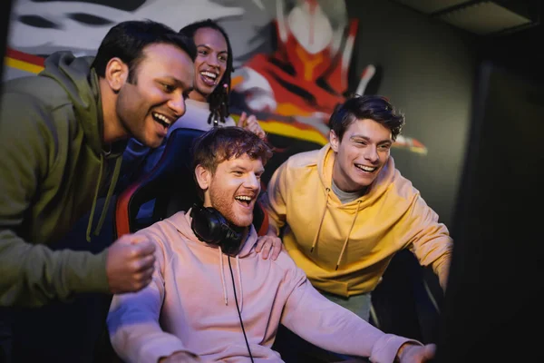 Cheerful multicultural friends playing computer game and rejoicing in gaming club — Stock Photo