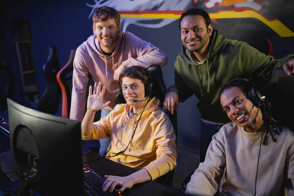 Smiling interracial friends looking at camera near computer in gaming club — Stock Photo