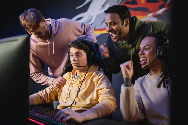 Excited interracial team looking at friend playing video game on computer in cyber club — Stock Photo