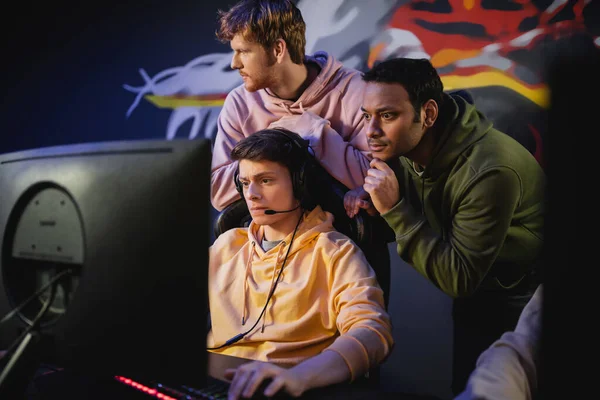Focused indian man standing near friend playing video game on computer in gaming club — Stock Photo