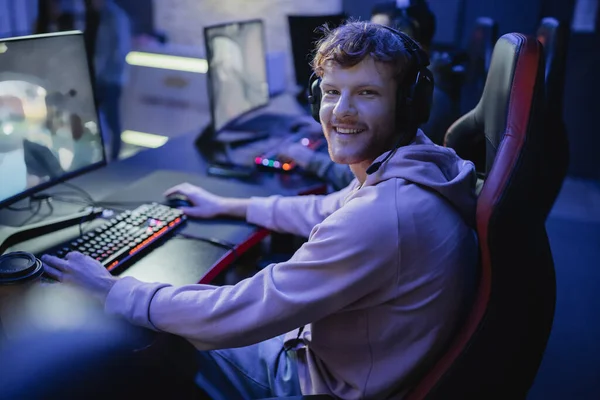 Jugador sonriente mirando a la cámara mientras juega videojuego en el club cibernético - foto de stock