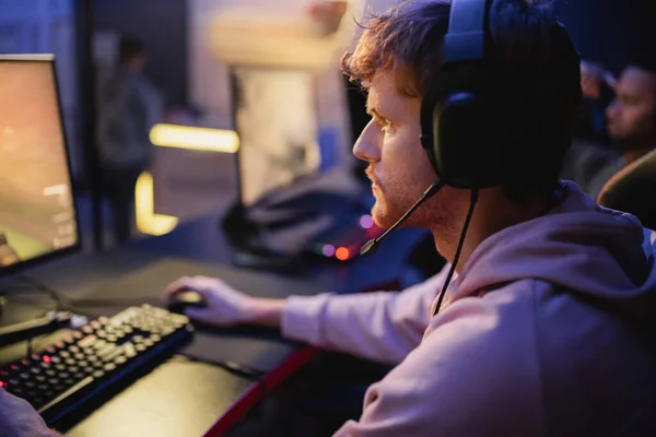 Боковой вид сфокусированного геймпада в наушниках, играющего видеоигру на компьютере в игорном клубе — стоковое фото
