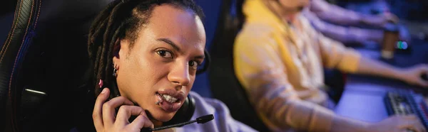 Multiracial gamer holding headphones and looking at camera in cyber club, banner — Stock Photo