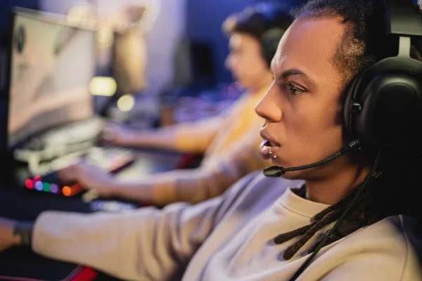 Vista lateral del jugador multirracial en auriculares con micrófono mirando hacia otro lado en el club de juegos - foto de stock