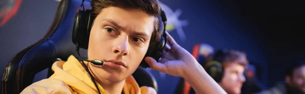 Joueur concentré dans les écouteurs avec microphone regardant loin dans le cyber-club, bannière — Photo de stock