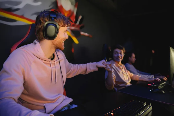 Fröhlicher Gamer mit Kopfhörern macht Faustschlag mit verschwommenem Freund in Spielclub — Stockfoto