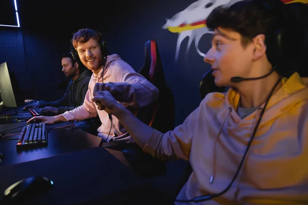 Smiling man doing fist bump with friend near keyboard in gaming club — Stock Photo