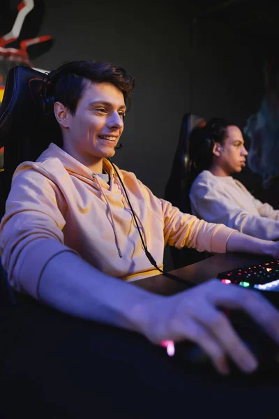 Giocatore sorridente con cuffie seduto vicino alla tastiera nel cyber club — Foto stock