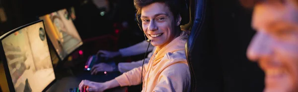 Jugador sonriente en auriculares mirando a un amigo borroso en blub de juegos, banner - foto de stock