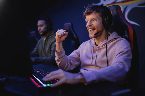 Emocionado jugador en auriculares con micrófono que muestra sí gesto cerca de la computadora en el club cibernético - foto de stock