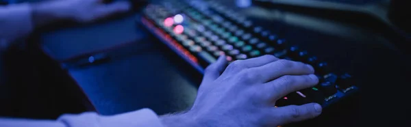 Vista recortada del hombre utilizando el teclado en el club cibernético con iluminación, bandera - foto de stock