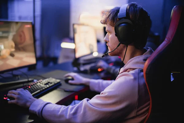 Side view of young gamer in headphones playing computer game in cyber club — Stock Photo