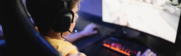 Гаджет в наушниках, играющий в видеоигру на компьютере в киберклубе, баннер — стоковое фото