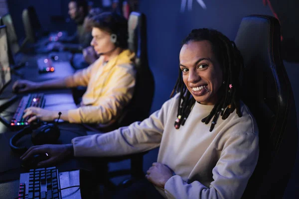 Multiracial gamer smiling at camera near blurred team in cyber club — Stock Photo