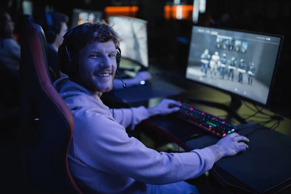 Carefree gamer in headphones playing video game on computer in cyber club with lighting — Stock Photo