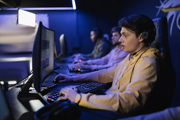 Вид збоку геймера в гарнітурі, гра з командою в кіберклубі — стокове фото