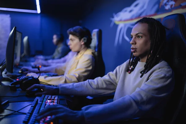 Мультирасовые геймеры играют в видеоигру с размытыми друзьями в киберклубе — стоковое фото