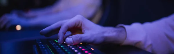 Vista recortada del jugador utilizando el teclado con iluminación en el club cibernético, bandera - foto de stock