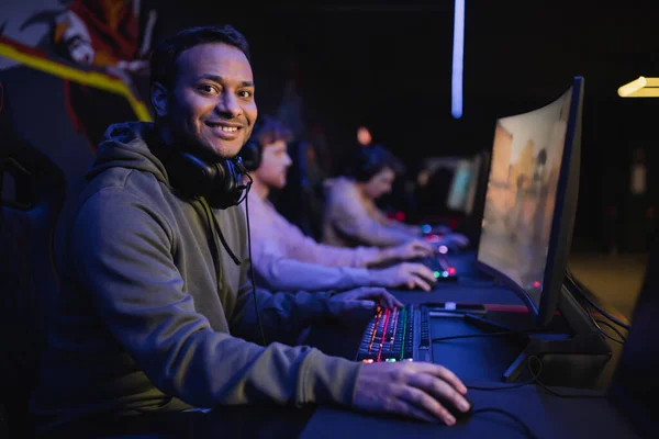 Lächelnder indischer Gamer blickt in Cyber-Club in Computernähe auf Kamera — Stockfoto