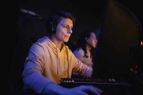Молодий чоловік в навушниках грає в комп'ютерну гру в кіберклубі з освітленням — стокове фото
