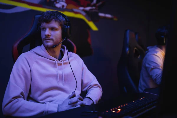 Young man in headphones looking away near blurred computer in cyber club — Stock Photo