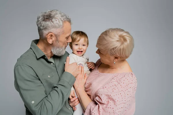 Безтурботний малюк дівчина дивиться на камеру біля бородатого дідуся і бабусі ізольовані на сірому — стокове фото