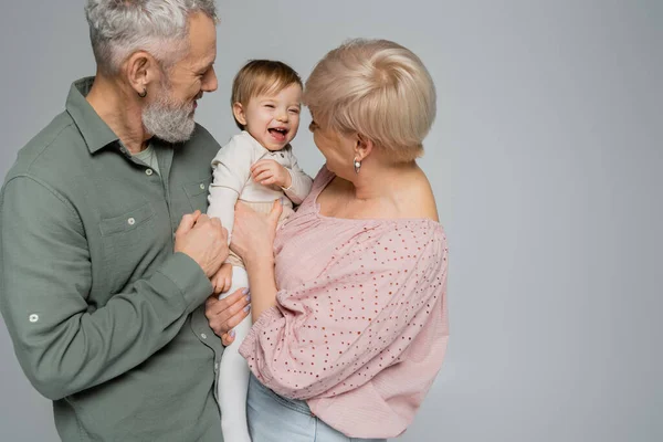 Mature couple embracing happy granddaughter laughing isolated on grey — Stock Photo
