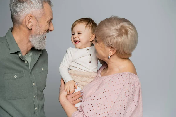 Бабушка держит счастливую внучку рядом с улыбающимся бородатым мужем, изолированным на серой — стоковое фото