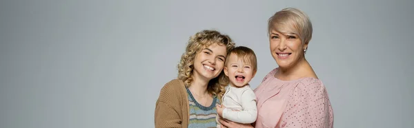 Excited baby girl laughing near happy mother and granny isolated on grey, banner — Stock Photo
