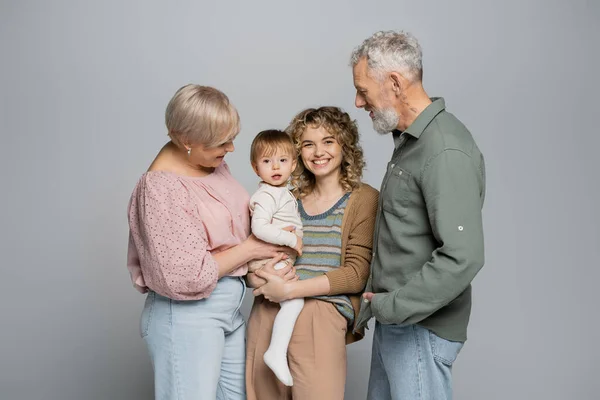 Pareja de ancianos mirando alegre hija adulta con niño pequeño aislado en gris - foto de stock