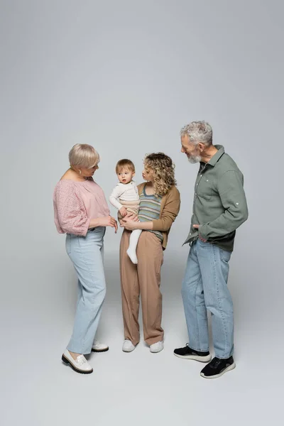 Полная длина женщины, держащей маленькую дочь рядом со счастливыми родителями на сером фоне — стоковое фото