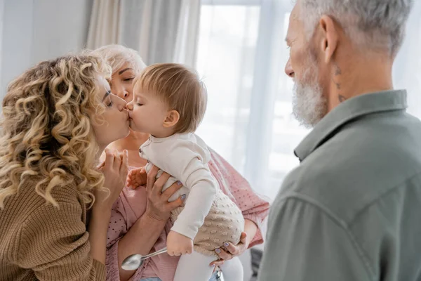 Blonde woman kissing beloved daughter near mature parents at home — Stock Photo