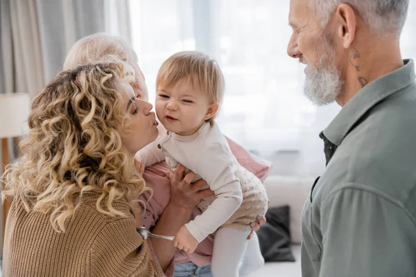 Блондинка кудрявая женщина целует дочь во время визита к зрелым родителям — стоковое фото
