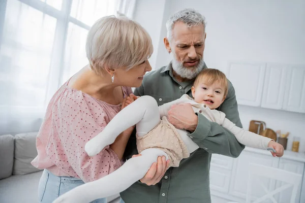 Carefree baby holding spoon near grandparents in kitchen — Stock Photo