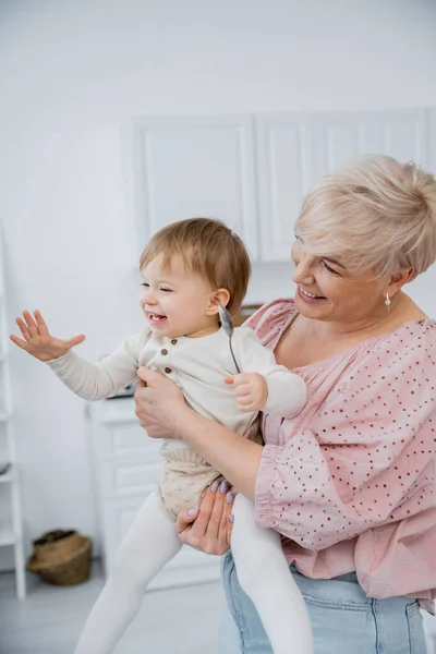 Feliz mulher madura abraçando animado neta segurando colher na cozinha — Fotografia de Stock