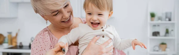 Lächelnde Frau umarmt unbeschwerte Enkelin in Küche, Banner — Stockfoto