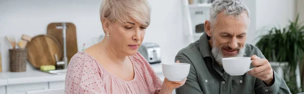 Женщина средних лет и улыбающийся бородатый мужчина пьет чай на кухне, баннер — стоковое фото