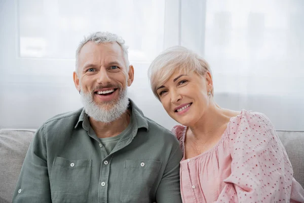 Felice uomo barbuto con moglie sorridente guardando la fotocamera a casa in soggiorno — Foto stock