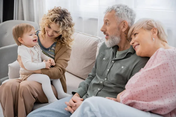 Smiling woman sitting with toddler daughter near happy parents on couch in living room — Stock Photo