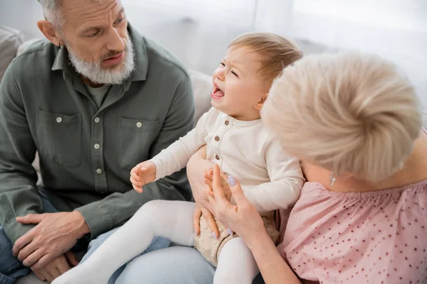 Offended child crying near discouraged grandparents on couch in living room — Stock Photo