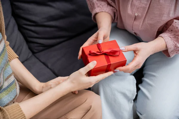 Cropped view of woman presenting gift to mature mother on couch at home — Stock Photo