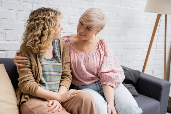 Cheerful middle aged woman with curly blonde daughter talking on couch in living room — Stock Photo