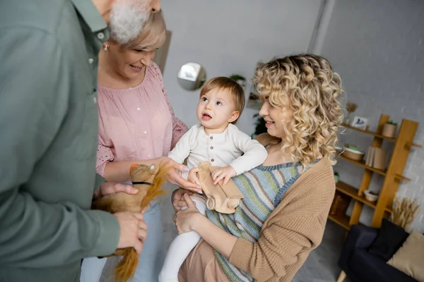 Здивована дівчина дивиться на бабусь і дідусів біля щасливої кучерявої матері у вітальні — стокове фото