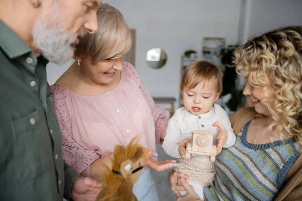 Little child looking at toy car near happy grandparents and mother in living room — Stock Photo