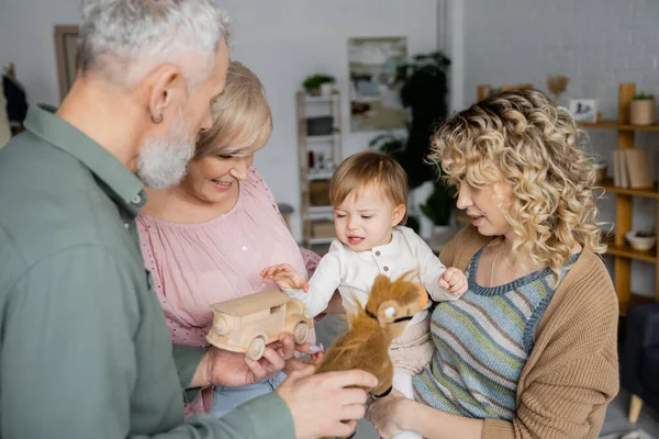 Бабусі і дідусі середнього віку тримають іграшки біля онуки малюка вдома — стокове фото