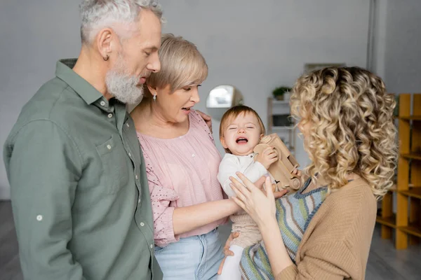 Offended child holding toy car and crying near mother and grandparents at home — Stock Photo