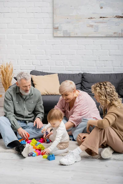 Glückliches Paar mittleren Alters spielt Bauklötzchenspiel mit Enkelin auf dem Fußboden im Wohnzimmer — Stockfoto